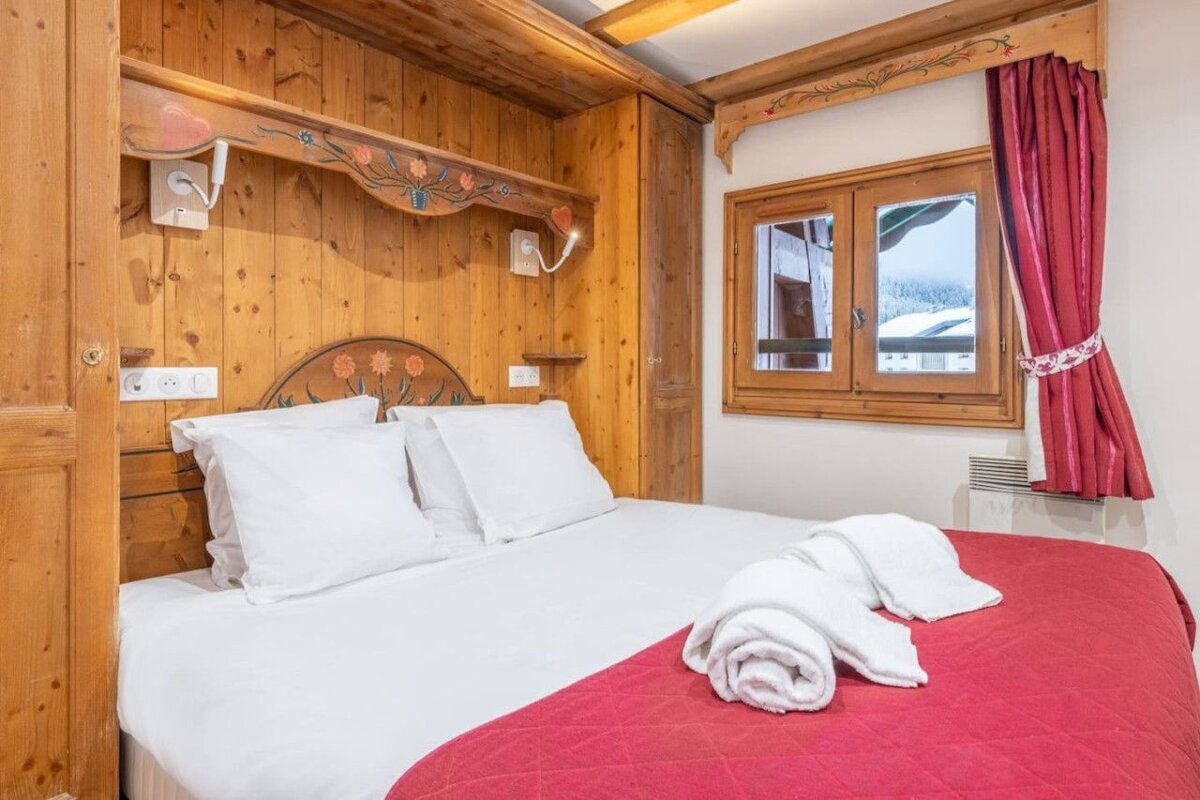 A bedroom with a bed and a window with a red curtain