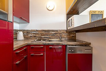 A compact kitchen with bright red cabinets, wood-textured backsplash/countertop, a sink, stove, microwave, and dishwasher.