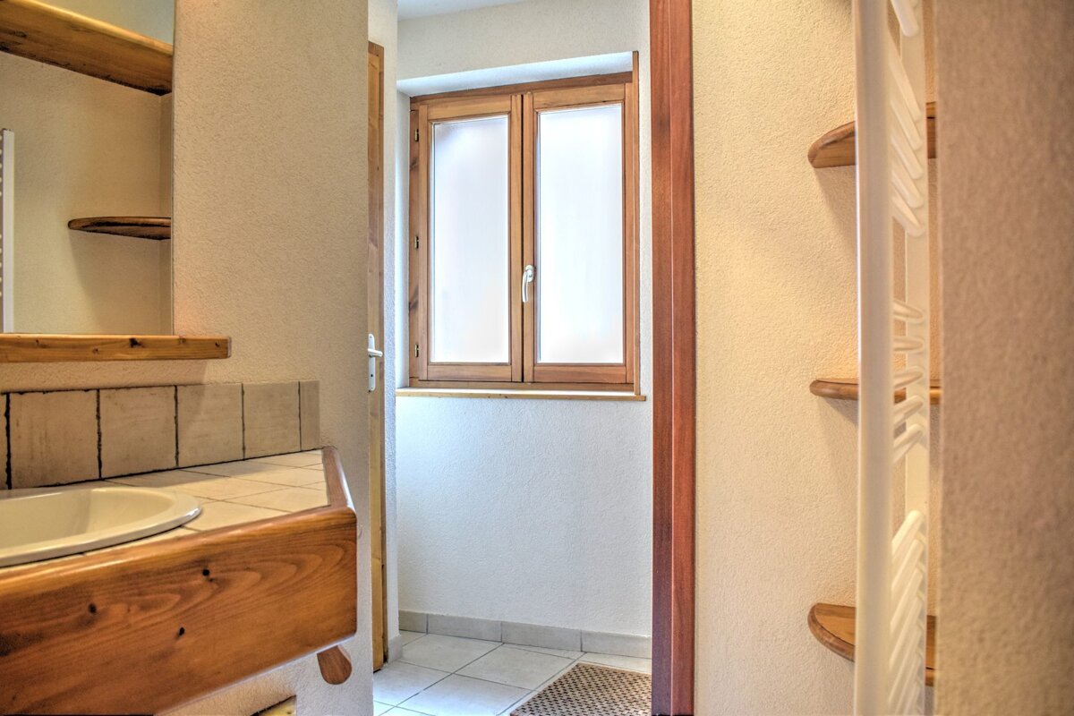 Rustic bathroom featuring a wooden sink vanity, tiled countertops, a frosted glass window, and built-in wooden shelves.