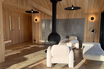 Cozy, modern wood-paneled room featuring a black suspended spherical fireplace, two plush white armchairs, and herringbone floors.