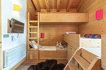 Cozy cabin bedroom made of light wood with built-in bunk beds, ladders, a wall-mounted TV, and a dark fluffy rug.
