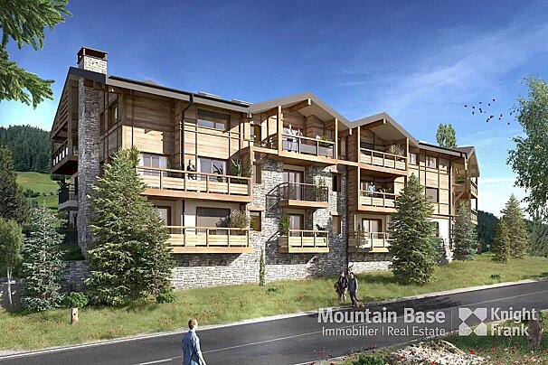 A large, modern wood and stone chalet-style building with multiple balconies, nestled in a green mountain landscape with pine trees under a clear blue sky, beside a road.