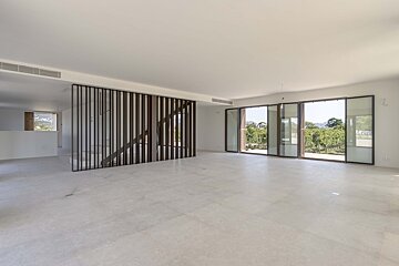 An empty, bright modern room with light-colored floors, a dark slatted partition, and large glass doors opening to a lush vineyard view.