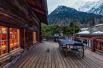 A wooden deck with a table and chairs and mountains in the background
