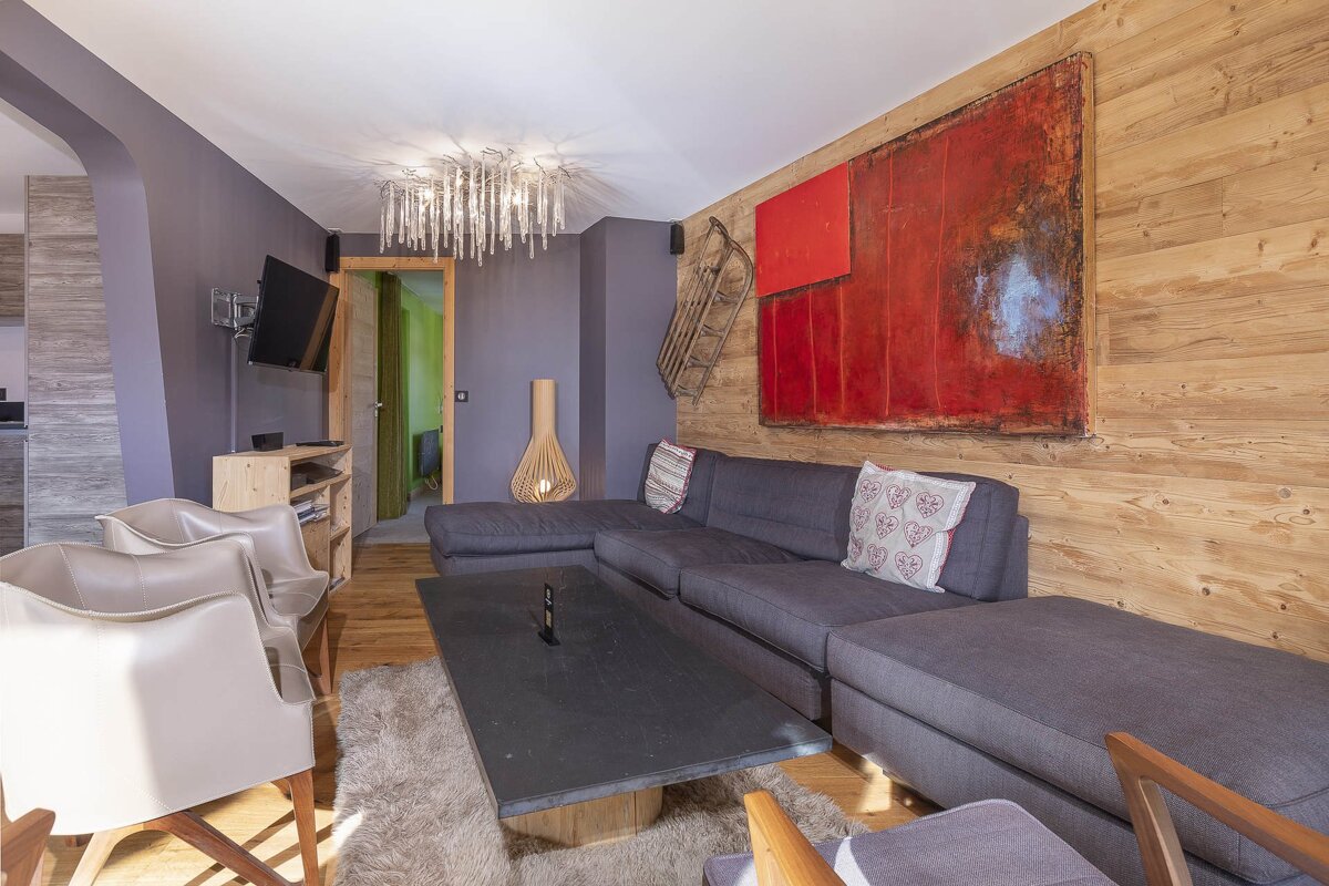 Chic living room with a grey sectional sofa, red abstract art on a wood-paneled wall, purple walls, and a modern chandelier.