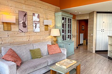 A cozy living room featuring wood-paneled walls, a grey sofa with colorful cushions, ski-themed art, and an orange ceiling.
