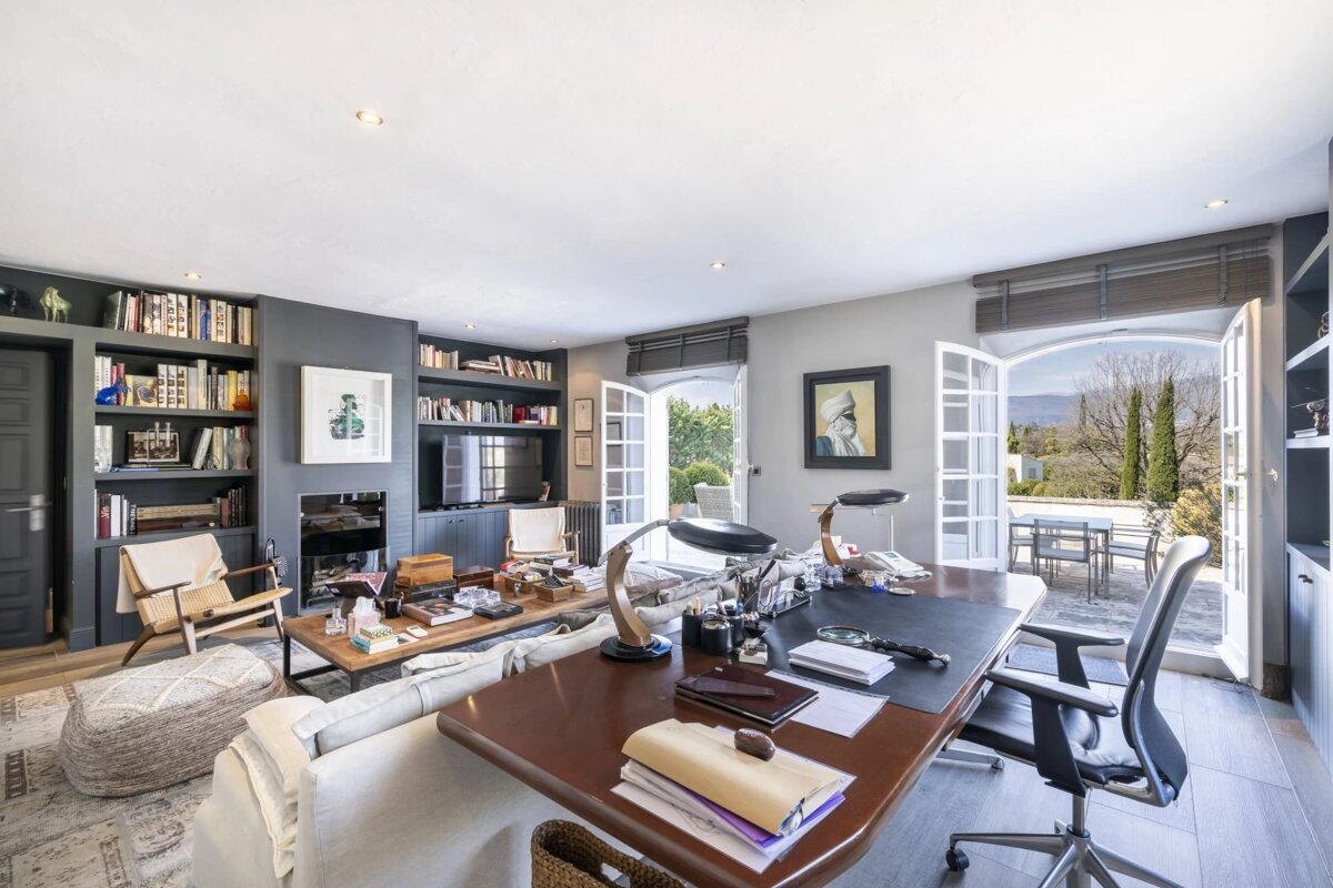 A spacious room featuring a study desk, lounge area with bookshelves, and open doors leading to a patio with scenic mountain views.
