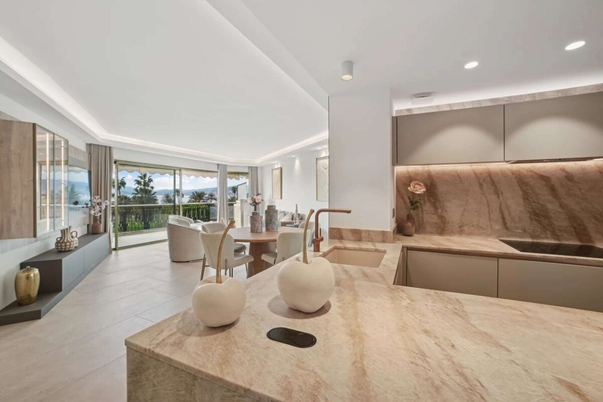 Chic open-plan kitchen and living area with luxurious marble, a dining table, and large windows revealing a scenic sea view.