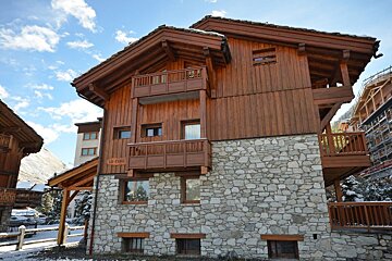 A wooden house with a stone wall and balconies has a sign that says le fort