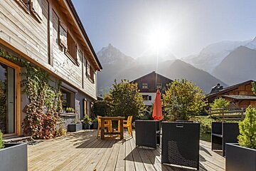 A wooden deck with a table and chairs and mountains in the background