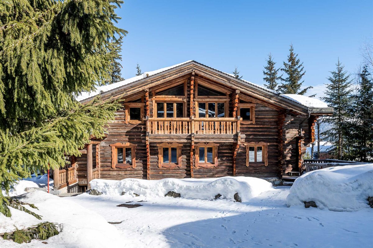 A large log cabin is surrounded by snow and trees