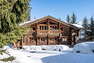 A large log cabin is surrounded by snow and trees