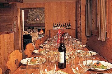 A bottle of wine sits on a table with plates and glasses