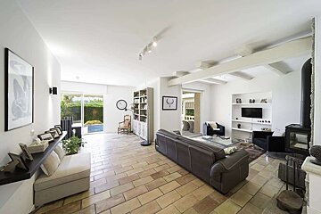 A bright, modern living room with terracotta floor tiles, a large leather sofa, fireplace, and sliding doors leading to an outdoor pool area.