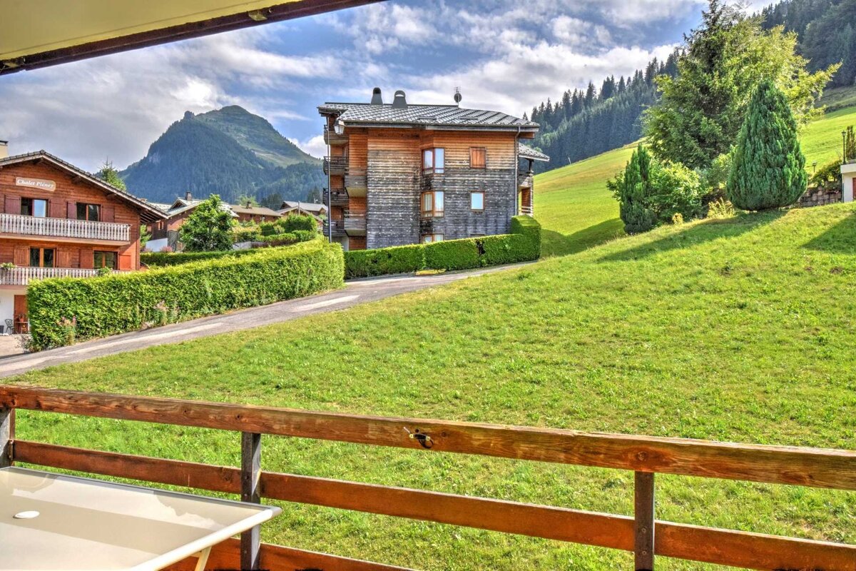 Balcony view of alpine chalets on green slopes with a majestic mountain in the background under a partly cloudy sky.