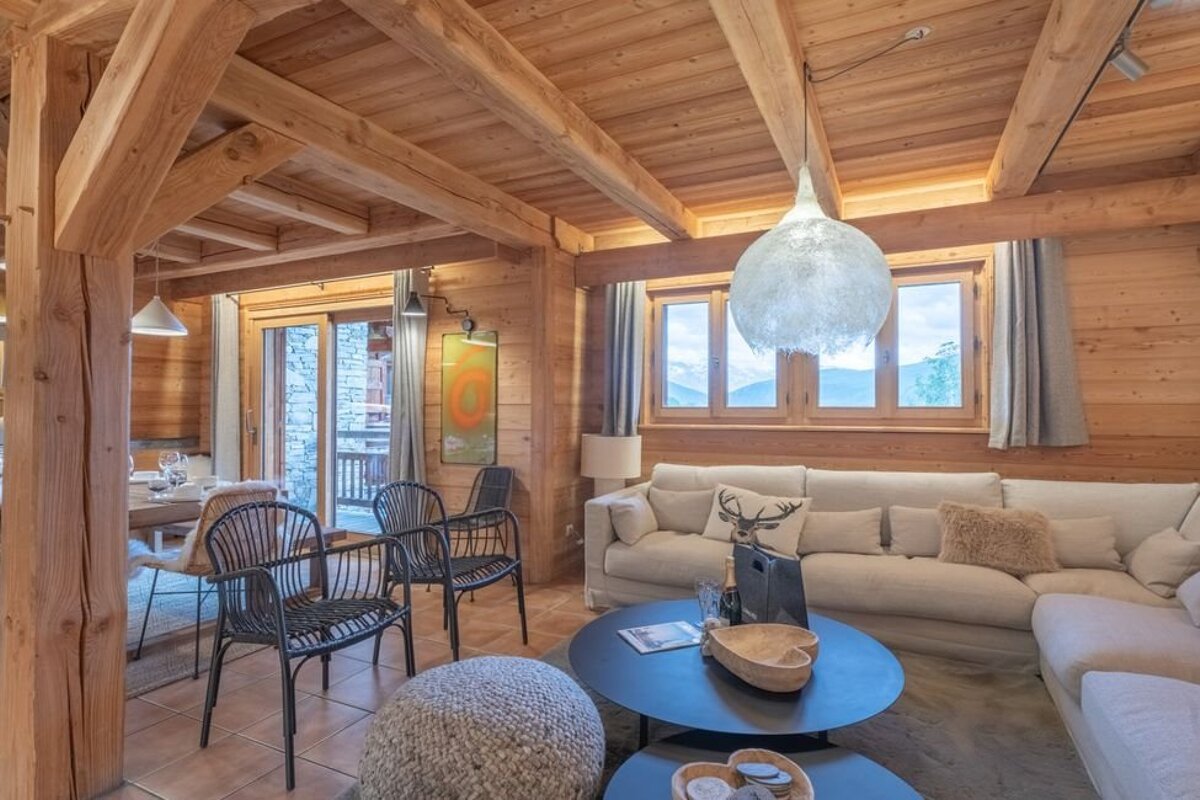 Cozy wooden chalet living room with a white sectional sofa, black armchairs, and a large spherical pendant light.