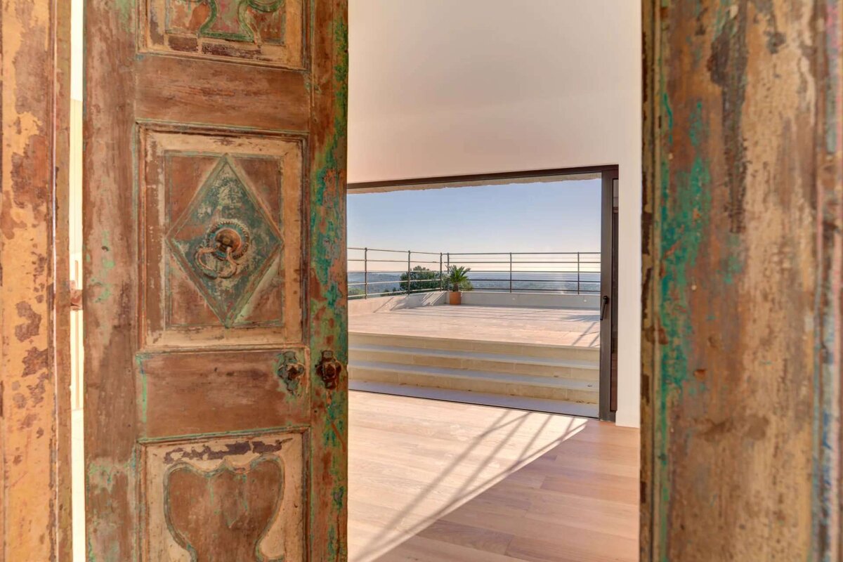 A wooden door open to a balcony with a view of the ocean
