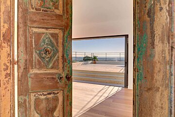 A wooden door open to a balcony with a view of the ocean