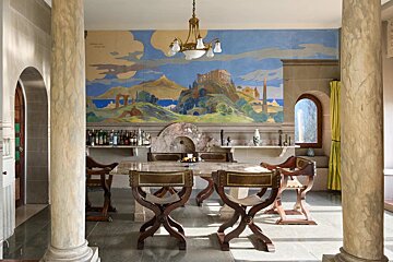Classical dining room with stone pillars, unique wooden chairs, and a large wall mural depicting ancient Greek ruins.