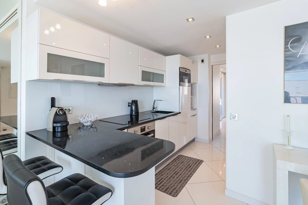 Modern white kitchen featuring glossy cabinets, a black countertop breakfast bar with stools, and integrated appliances.