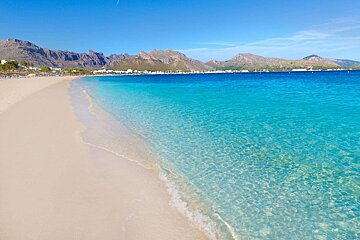 A beach with clear water and mountains in the background