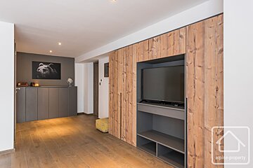 Modern hallway features wooden floors, a grey console with bear art, and a full-wall rustic wood unit integrating a TV and shelving.
