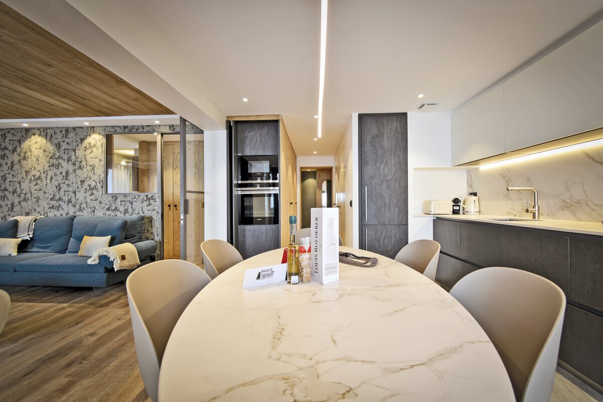 Chic open-plan apartment with a marble dining table, blue sofa, and modern kitchen. Features sleek built-in appliances, wood flooring, and ambient lighting.