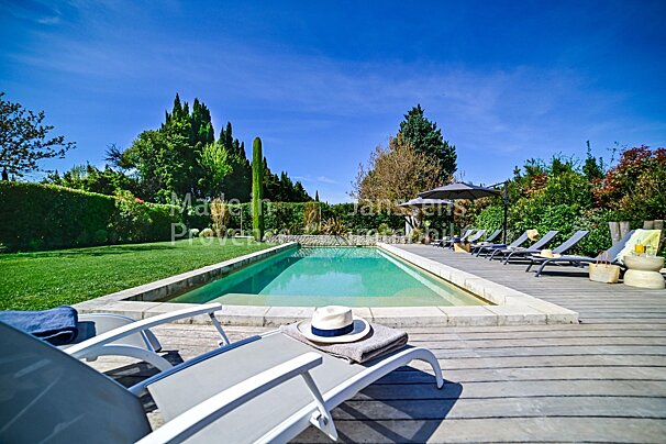 A large swimming pool is surrounded by lawn chairs and umbrellas with the words made in provence visible in the background