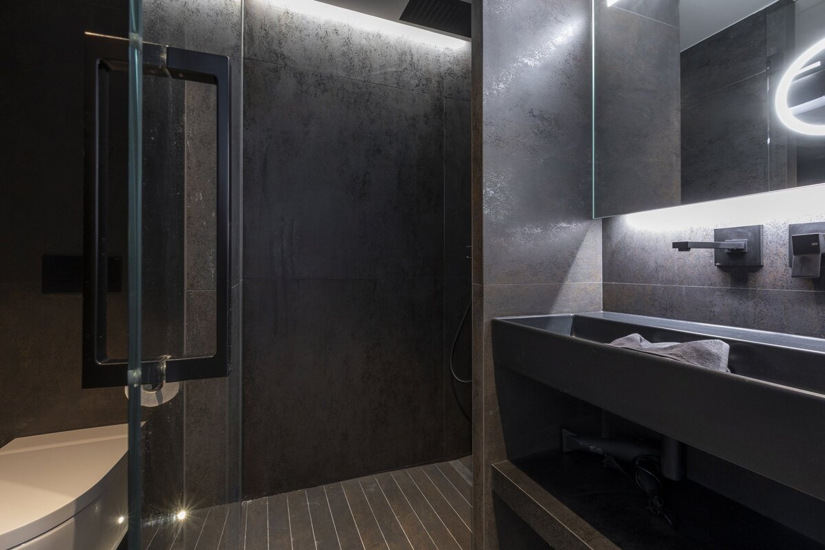 Modern dark grey bathroom featuring a walk-in shower and a sleek black vanity under a backlit mirror.