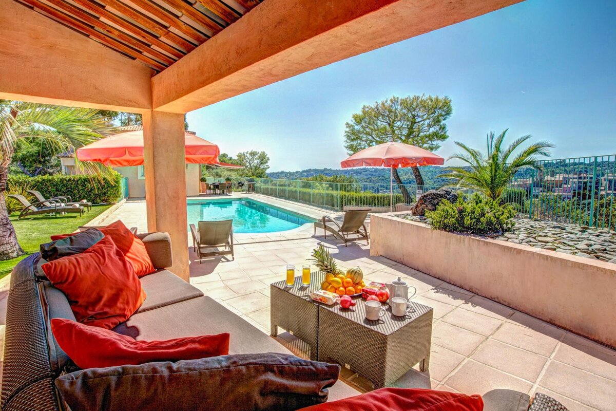 A patio with a couch and umbrellas overlooking a pool