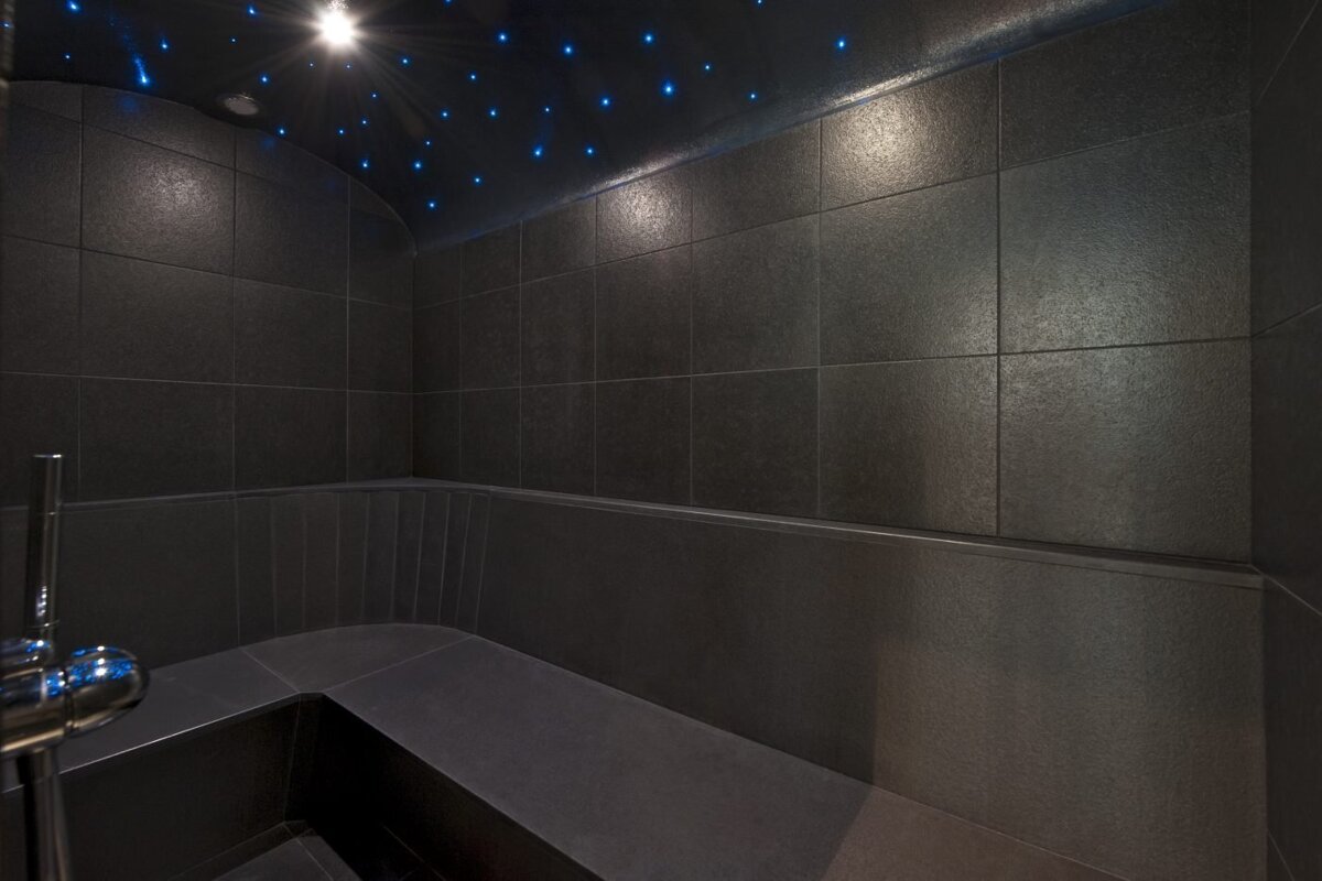 A bathroom with black tiles and blue lights on the ceiling