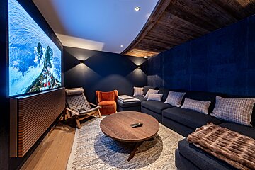 A modern, dark blue media room featuring a large TV, comfortable sectional sofa, and accent chairs, centered around a round coffee table.