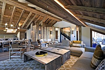 A modern rustic chalet interior with a vaulted wooden ceiling, open living and dining space, warm lighting, and elegant contemporary furnishings.