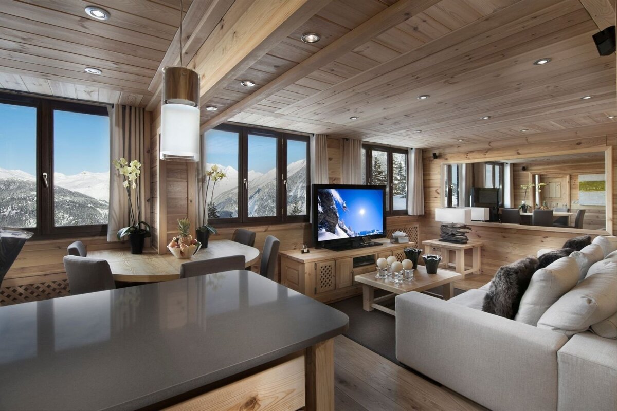 Cozy wood-paneled chalet with living & dining areas. Large windows frame stunning snowy mountain views, creating a warm, modern alpine retreat.