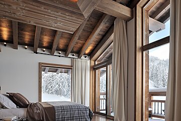 A bedroom with a large window and a bed with a plaid blanket on it