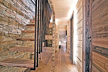 Rustic wooden hallway featuring a floating staircase set against a stone wall in a cozy cabin interior.