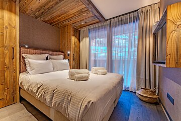 A bedroom with a wooden ceiling and white curtains