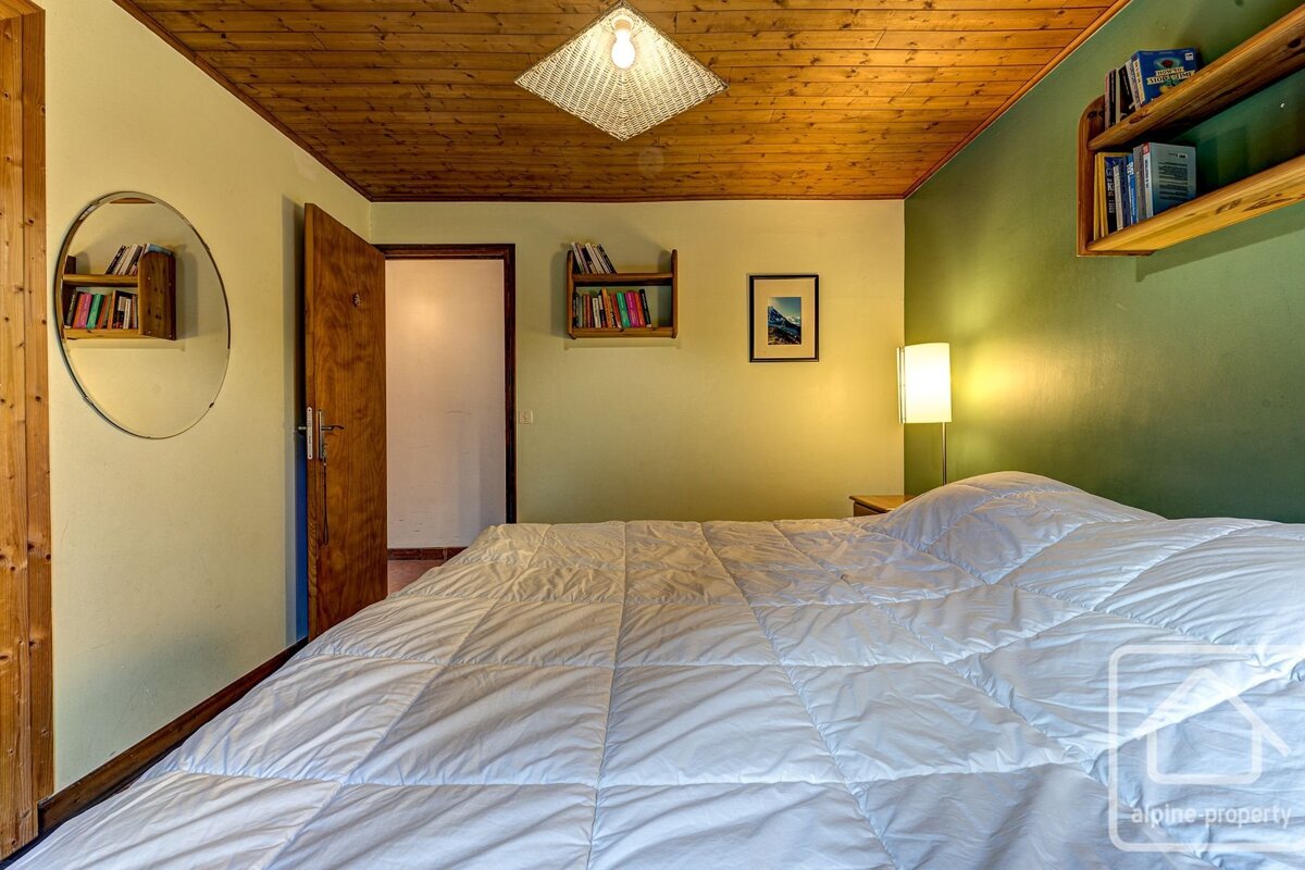 Bedroom with wood ceiling, green accent wall, white-quilted bed, circular mirror, and built-in bookshelves.