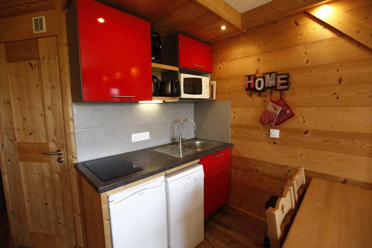 A cozy, wood-paneled kitchen with bright red cabinets, a sink, modern appliances, and a