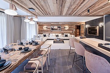 A modern chalet interior featuring a wooden dining table, a cozy living area with a white sectional, and a sleek bar._
