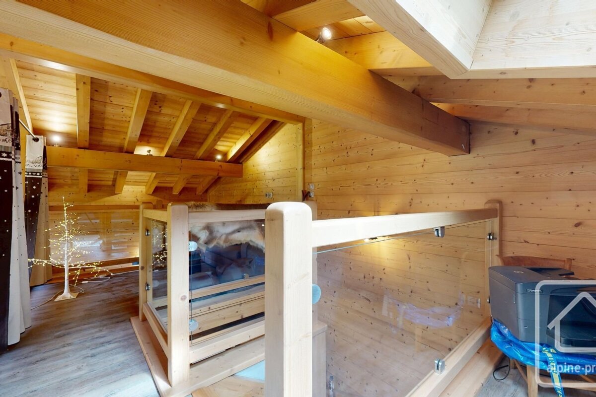 Rustic wooden chalet loft featuring exposed beams, glass railings, and an illuminated decorative tree, creating a warm ambiance.