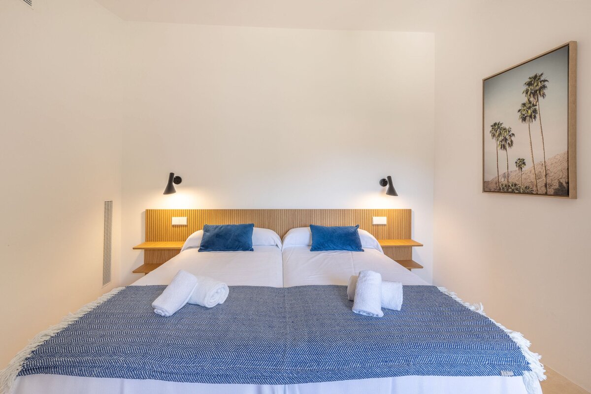 A bedroom with two beds and a picture of palm trees on the wall