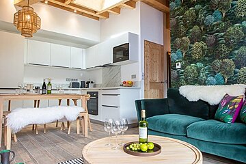 Stylish apartment featuring a green velvet sofa, a tree-patterned wall, and a wooden dining set next to a modern white kitchen.