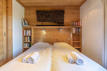 A bedroom with two beds and a shelf with books on it