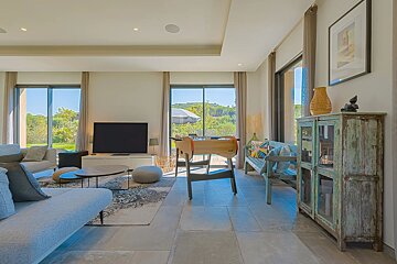 A spacious, sunlit living room featuring modern sofas, a TV, a foosball table, and rustic decor overlooking a bright garden.