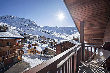 A balcony overlooking a snowy village with mountains in the background