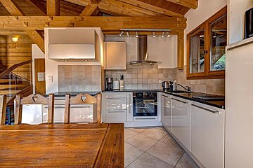 Modern kitchen with sleek light cabinets, tiled backsplash & floor, contrasted by rustic wooden beams & a dining table with heart-cutout chairs.