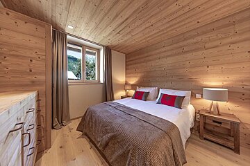 Warm, wood-paneled bedroom with a large bed, two lamps, and a window overlooking a green, hilly landscape. Cozy and natural aesthetic.