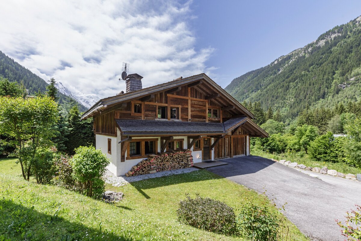 A house in the mountains with a pile of logs in front of it