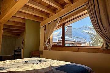 A cozy bedroom with a wooden beamed ceiling and a window showcasing a breathtaking snowy mountain and chalet view.